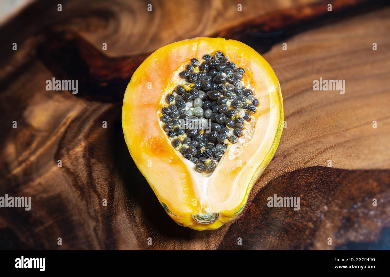 Ein gelber Papaya auf einem Holztisch Hintergrund. Nahaufnahme der Samen eines Papaya. Makrofotografie der tropischen exotischen Frucht. Die Hälfte der reifen Papaya f Stockfoto