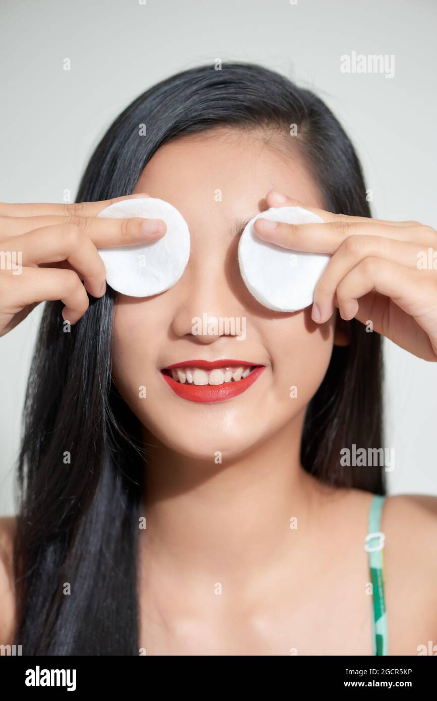 Hübsche Schönheit junge asiatische Frau, die ihre Augen mit Wattepad über weißem isolierten Hintergrund bedeckt. Gesundes Haut- und Kosmetikkonzept. Stockfoto