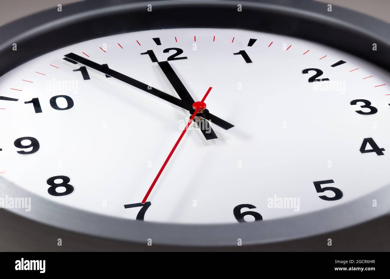 Es ist fünf bis zwölf, die Uhr tickt. Moderne Wanduhr zeigt die Zeit 5 vor 12 an. Nahaufnahme einer Wanduhr, mit fünf Minuten bis zwölf Uhr Stockfoto