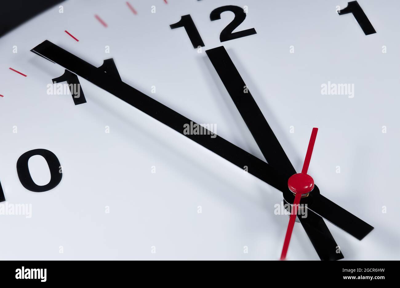 Es ist fünf bis zwölf, die Uhr tickt. Moderne Wanduhr zeigt die Zeit 5 vor 12 an. Nahaufnahme einer Wanduhr, mit fünf Minuten bis zwölf Uhr Stockfoto