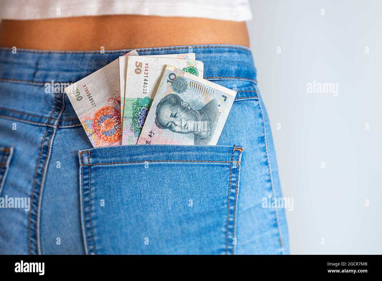 100 Chines Yuan in einer weiblichen Jeanstasche. China-Banknoten stecken in einer Jeans-Tasche. Renminbi in der Gesäßtasche einer Denim-Hose für Mädchen oder Frauen. Stockfoto