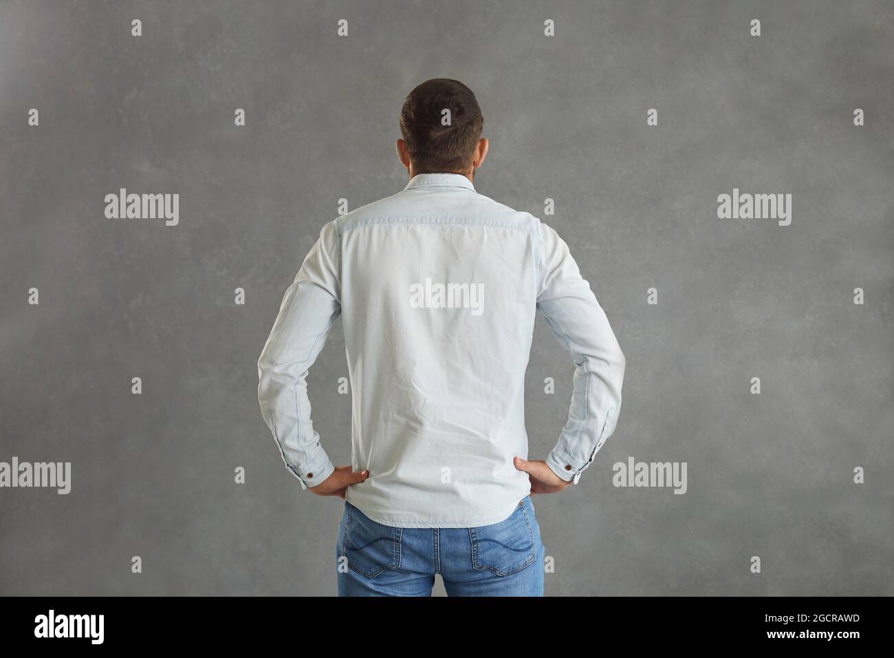 Rückansicht des Mannes im Denim-Hemd, der Hände auf Hüften auf grauem Hintergrund isoliert hält Stockfoto