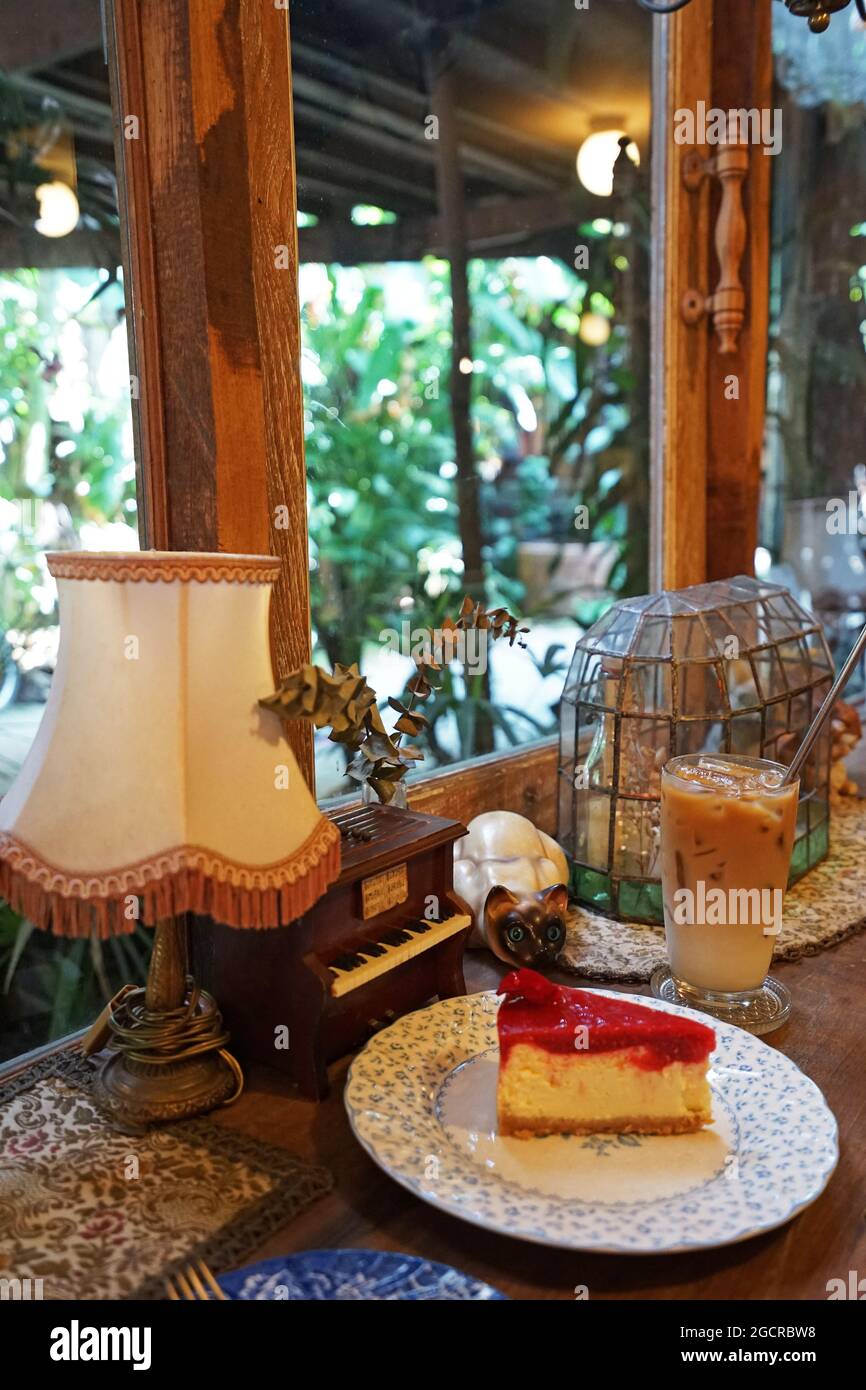 Erdbeer-Käsekuchen, serviert mit einem Glas vereisten Latte-Kaffee in einem Vintage-Café, das mit antiken Holzmöbeln eingerichtet ist Stockfoto