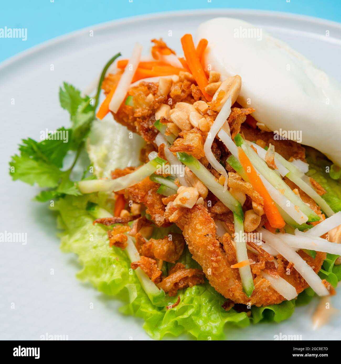 Köstliches gedämpftes bao-Brötchen auf einem Teller mit gebratenem Huhn und frischem Gemüse - Salat, Karotten und gerösteten Erdnüssen. Beliebtes Street Food Stockfoto