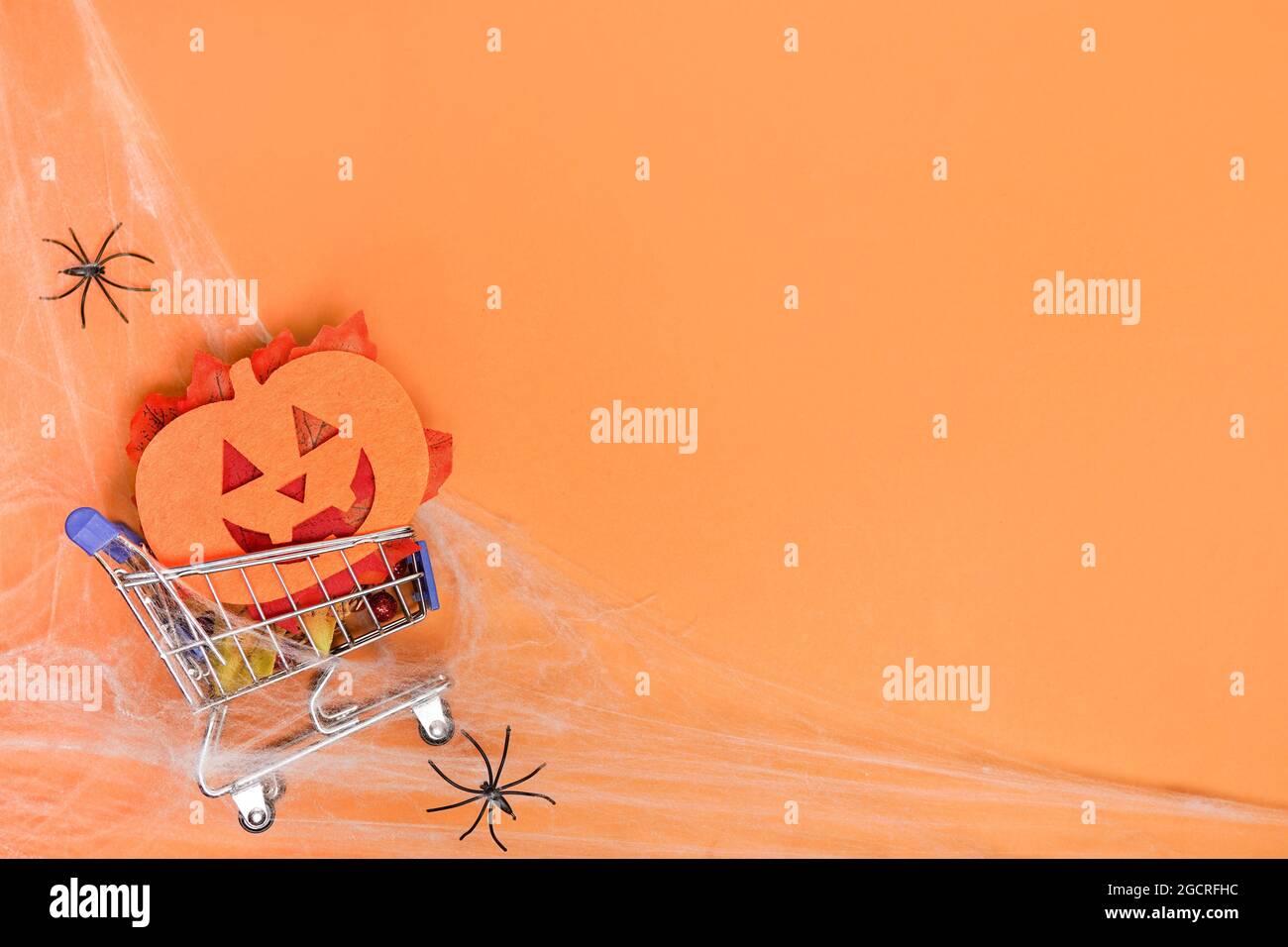 Einkaufswagen mit dekorativem Kürbis, Spinnen auf orangefarbenem Hintergrund. Flach legen Halloween . Halloween Verkaufskonzept. Platz kopieren Stockfoto