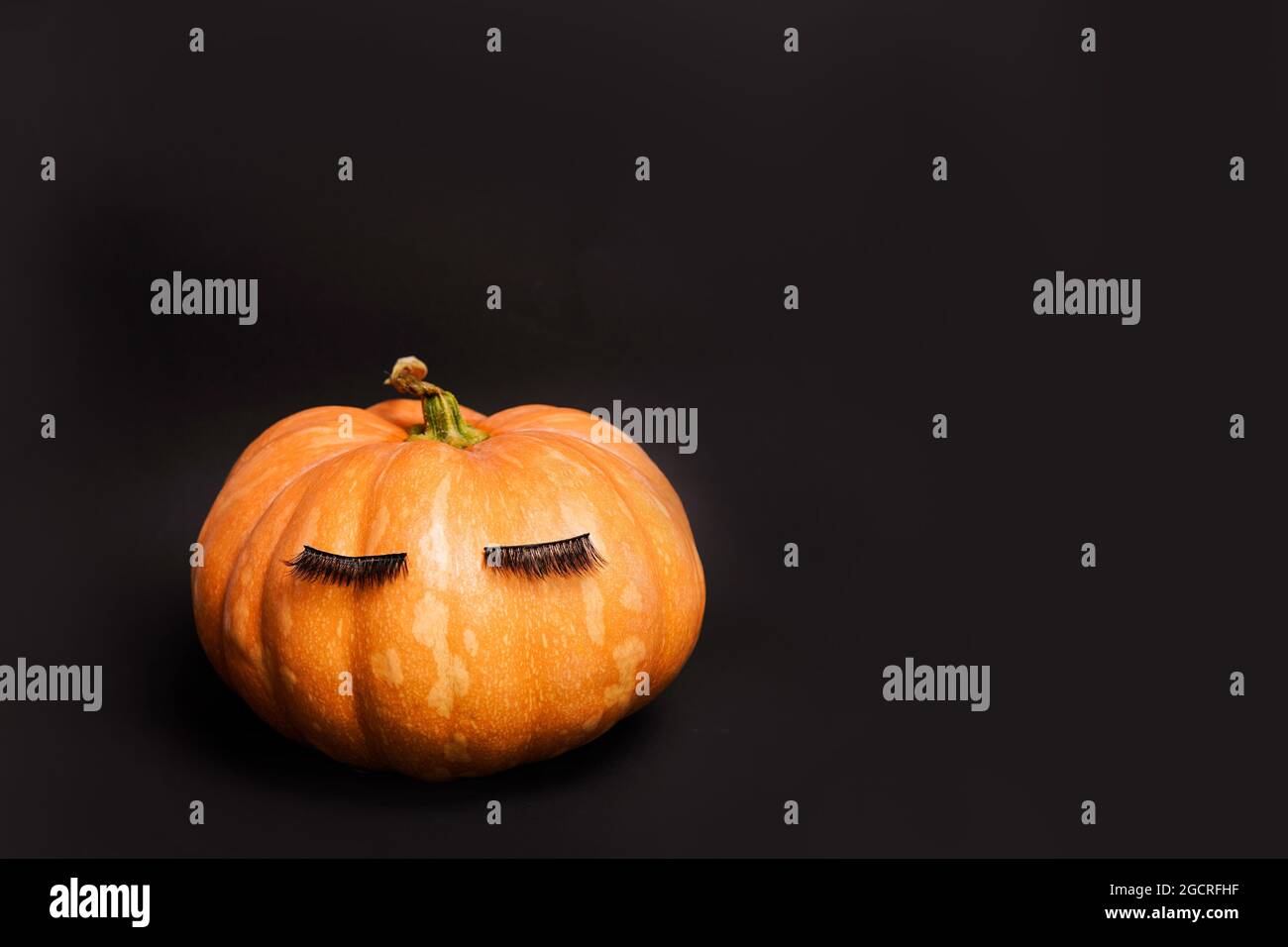 Kürbis mit falschen Wimpern auf schwarzem Hintergrund. Herbst, Herbst, halloween-Konzept. Copy Space Stockfoto