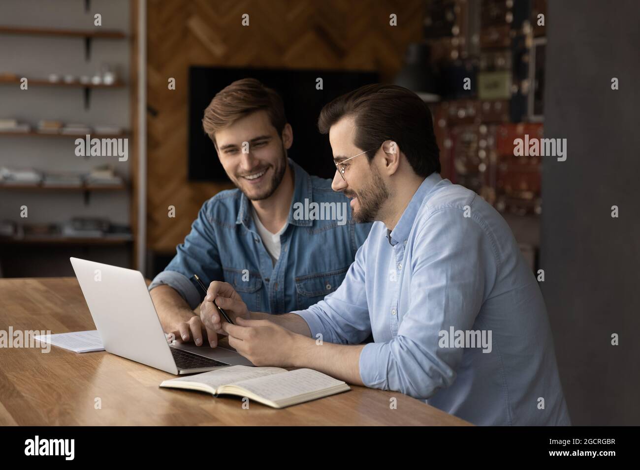 Glückliche männliche Kollegen, die sich einen Laptop teilen und über das Projekt sprechen Stockfoto