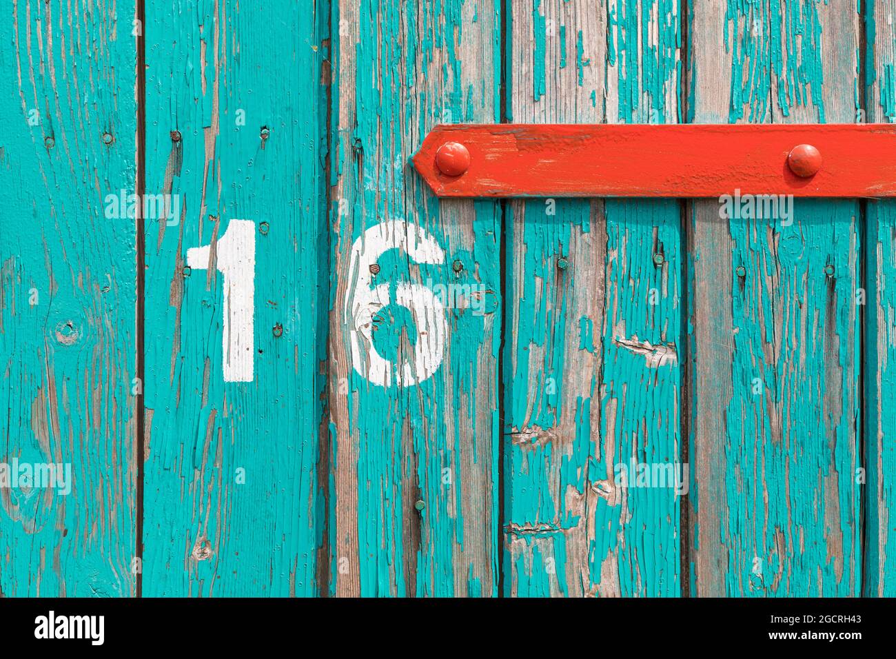 Verwitterte Türe aus Holz mit rotem Fitting und abstraktem Hintergrund mit der Nummer 16 Stockfoto