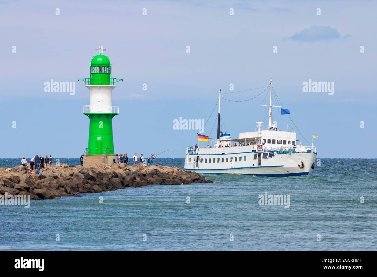 Ausflugsboot am grünen Leuchtturm an der Spitze des Wellenbrechers des Hafens von Warnemünde vorbei. Stockfoto