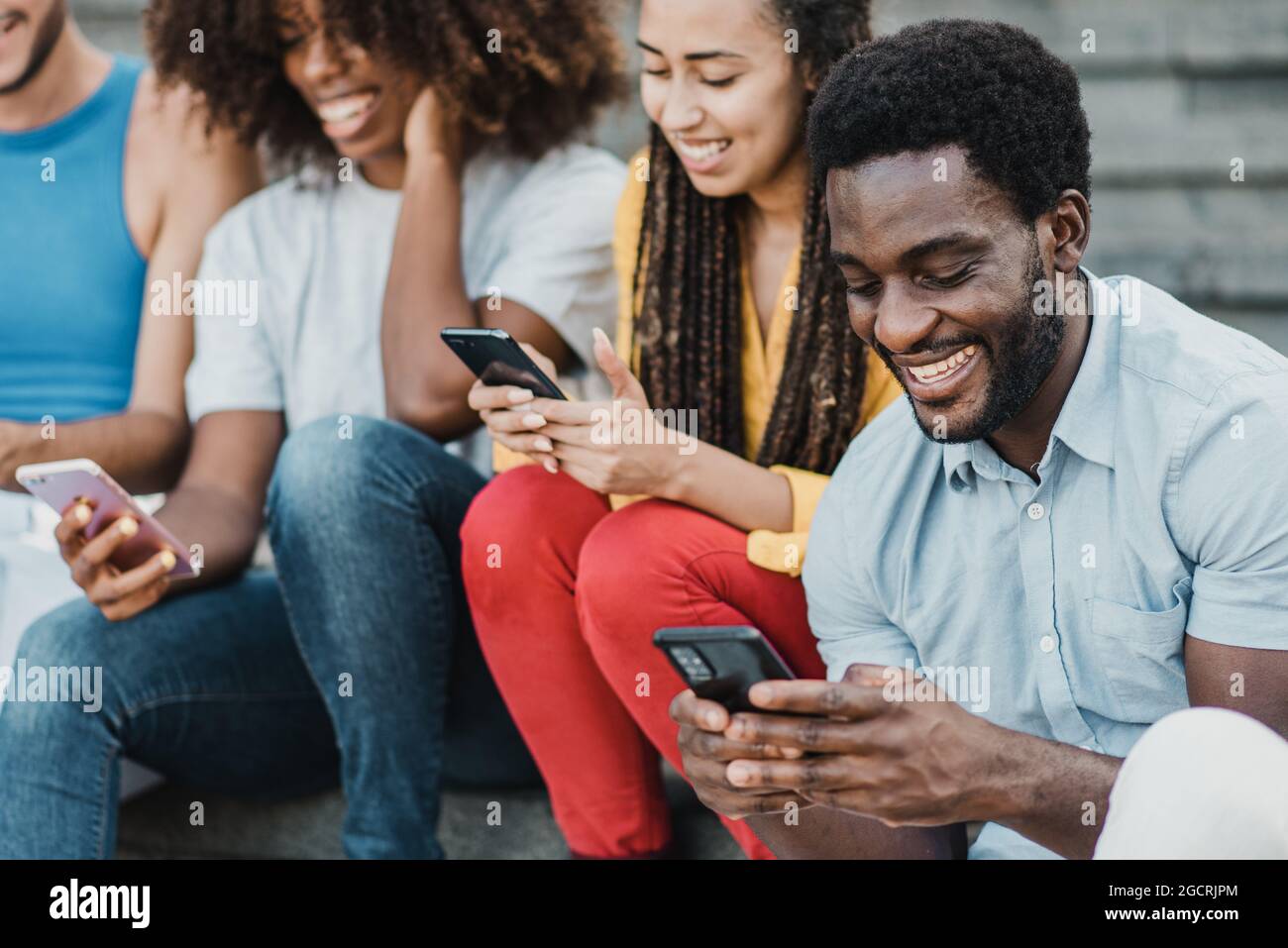 Multirassische Menschen, die Spaß mit Mobiltelefonen im Freien in der Stadt - Fokus auf afrikanischen Mann Gesicht. Stockfoto