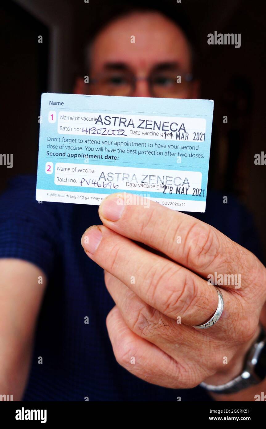 Mann hält eine Impfkarte mit beiden Marken des Astra Zeneca-Impfstoffs mit weichem Fokus hoch. Stockfoto