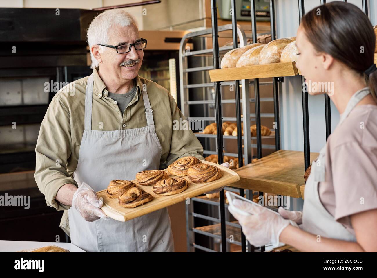 Glücklicher älterer Mann mit Brötchen und seine Tochter mit Tablet, die in der Bäckerei arbeitete Stockfoto