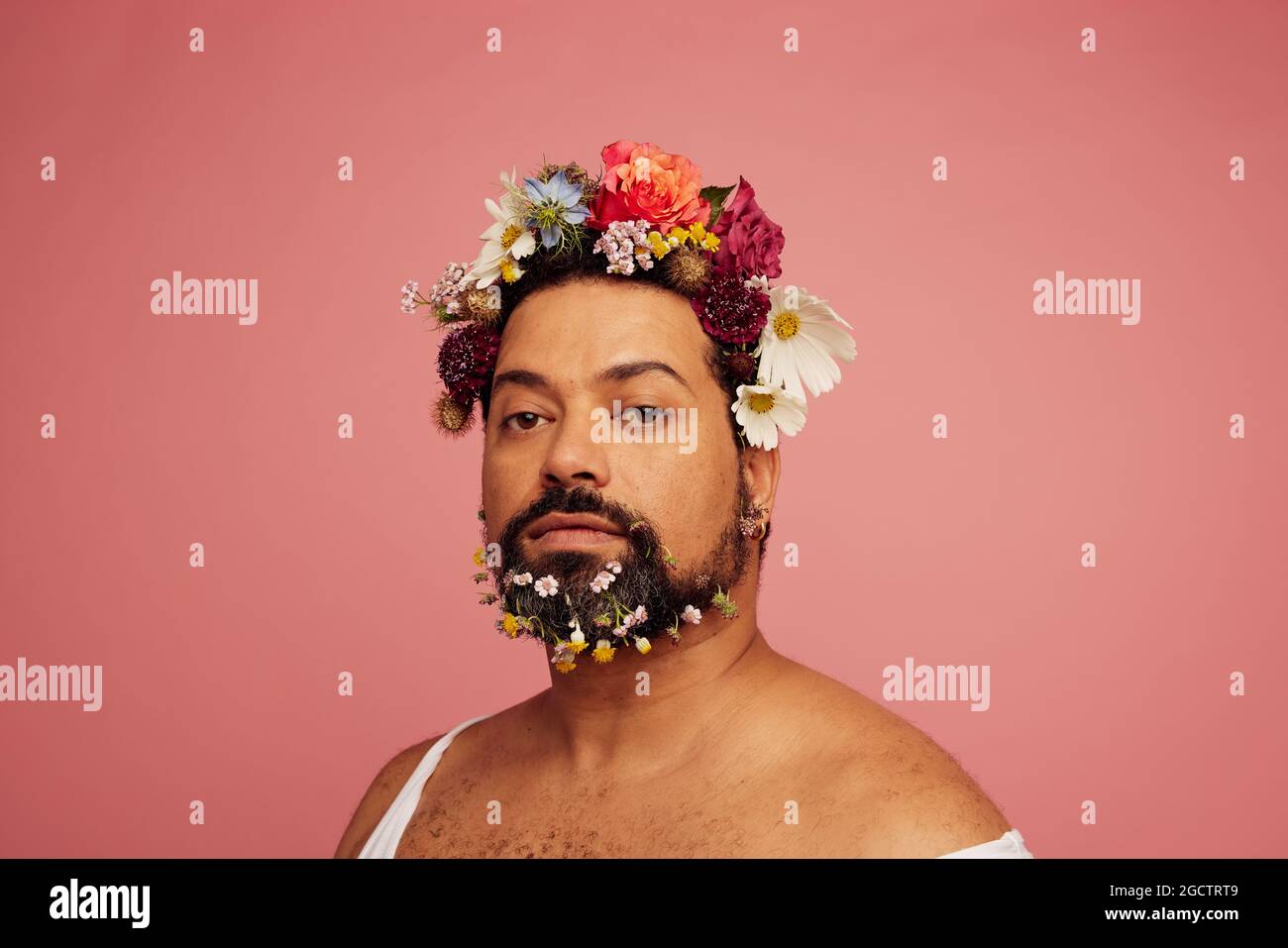 Androgyne männliche mit Blumen Make-up. Bärtiger Rüde mit floralem Make-up auf rosa Hintergrund. Stockfoto