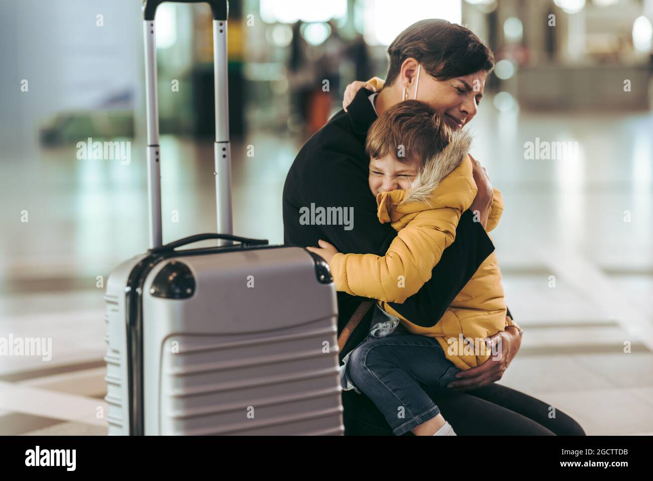 Mutter mit ihrem Kind am Flughafen in einer Pandemie am Flughafen. Frau fühlt sich emotional, als sie ihren Sohn während des Covid-19-Ausbruchs am Flughafen trifft. Stockfoto
