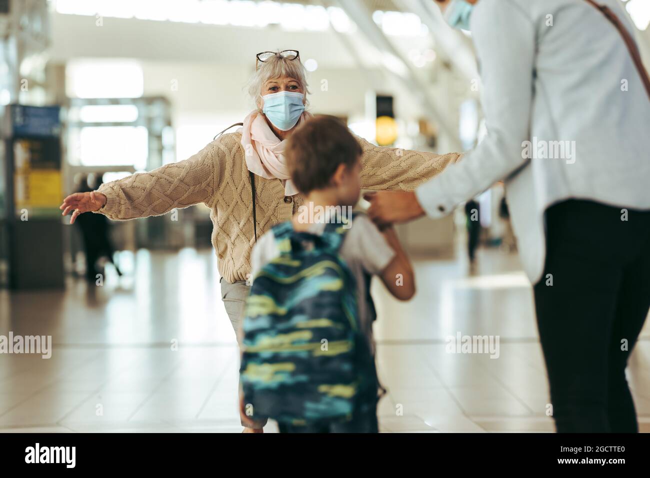 Eine ältere Frau begrüßt ihre Tochter und ihr Kind mit offenen Armen am Ankunftseingang des Flughafens. Großmutter begrüßte ihr Enkelkind und ihre Tochter am Flughafen Stockfoto