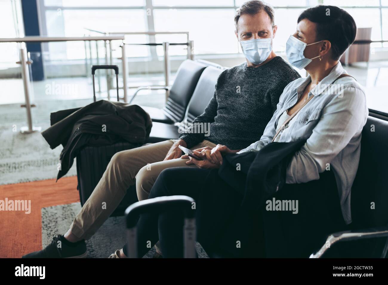 Ein Paar mit Gesichtsmasken sitzt am Flughafen. Mann und Frau, die während einer Pandemie des Covid-19 unterwegs waren. Stockfoto