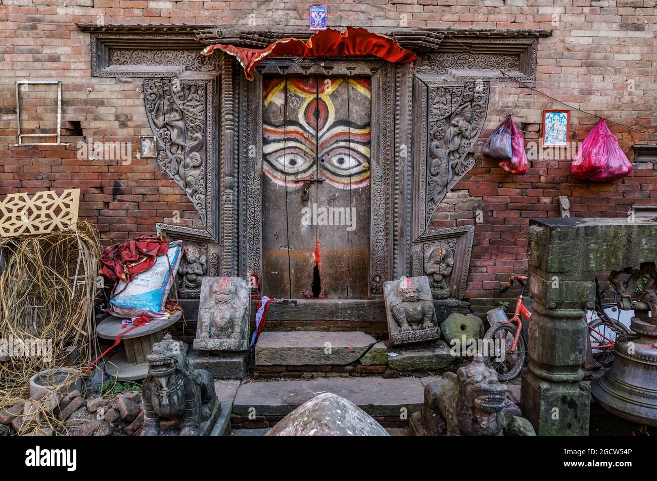 Eine Holztür mit bemalten Buddha-Augen und geschnitzten Ornamenten an einer roten Backsteinmauer, traditionelle nepalesische Architektur in Kathmandu, Nepal Stockfoto