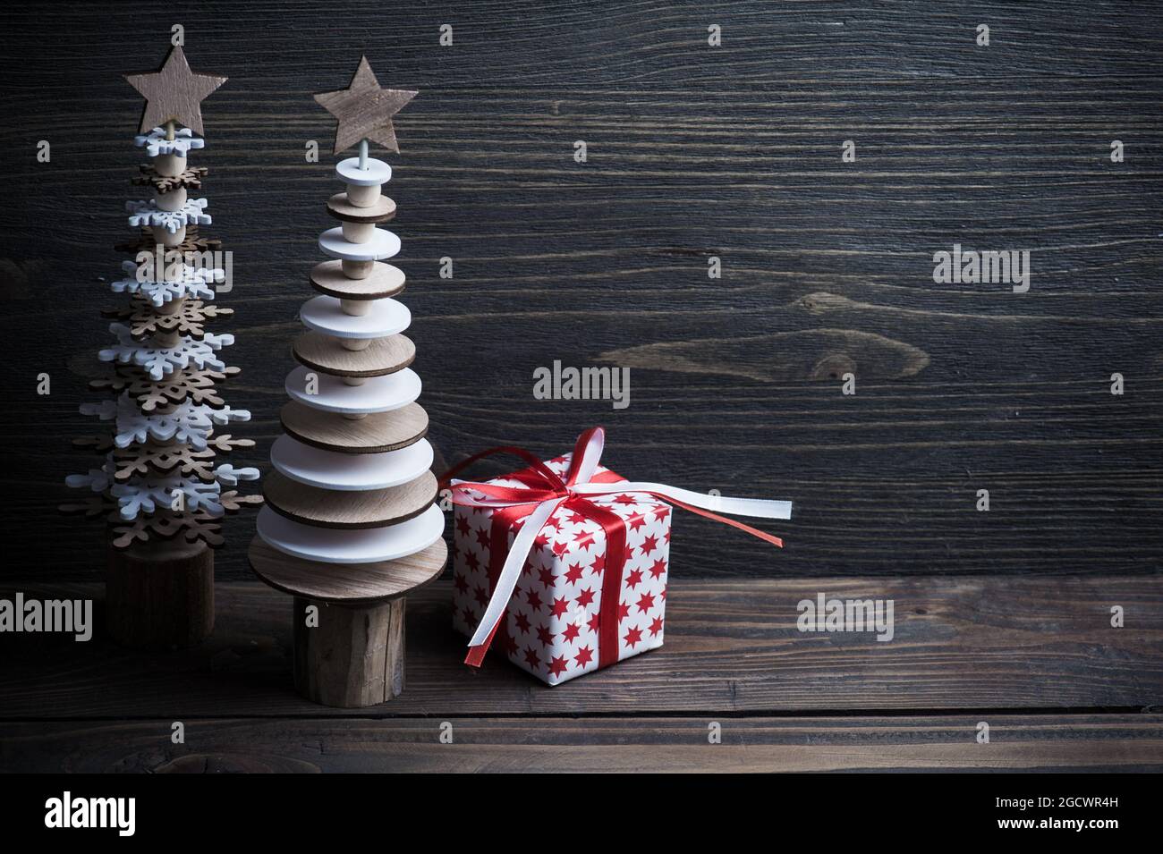 Weihnachten Holzbäume und weiße rote Geschenkbox vover dunklen rustikalen Holzhintergrund. Öko-Stil, Naturholz, Platz für Text. Getöntes Bild Stockfoto