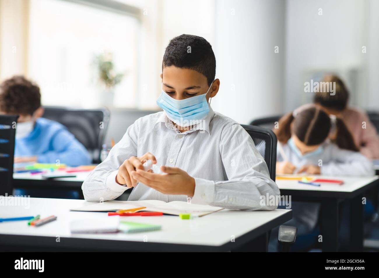 Kleiner männlicher Student, der antibakterielle Desinfektionsmittel auf die Hände aufgibt Stockfoto