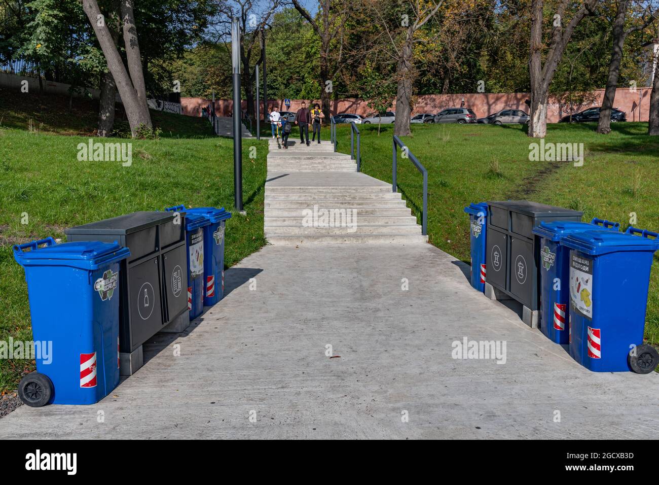 Bürgersteig und Treppen im Park mit Abfallrecyclingkannen für sortierten Müll an den Seiten auf dem Rasen. Nachhaltiger Lebensstil im urbanen Umfeld. Umgebung c Stockfoto