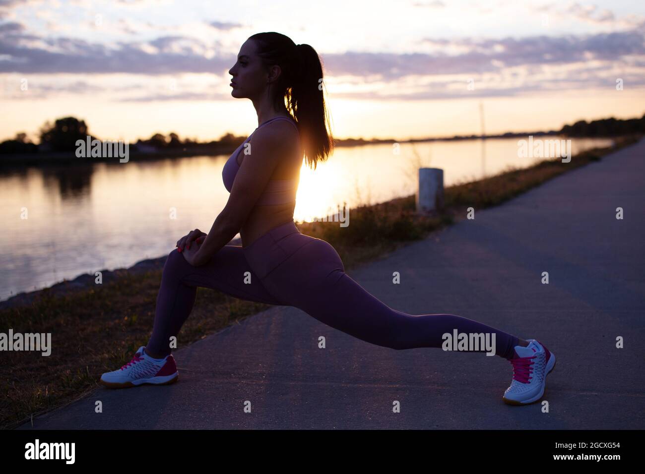 Junge Frau Silhouette macht Stretching Aufwärmübungen, bevor sie am Morgen am Flussufer läuft Stockfoto