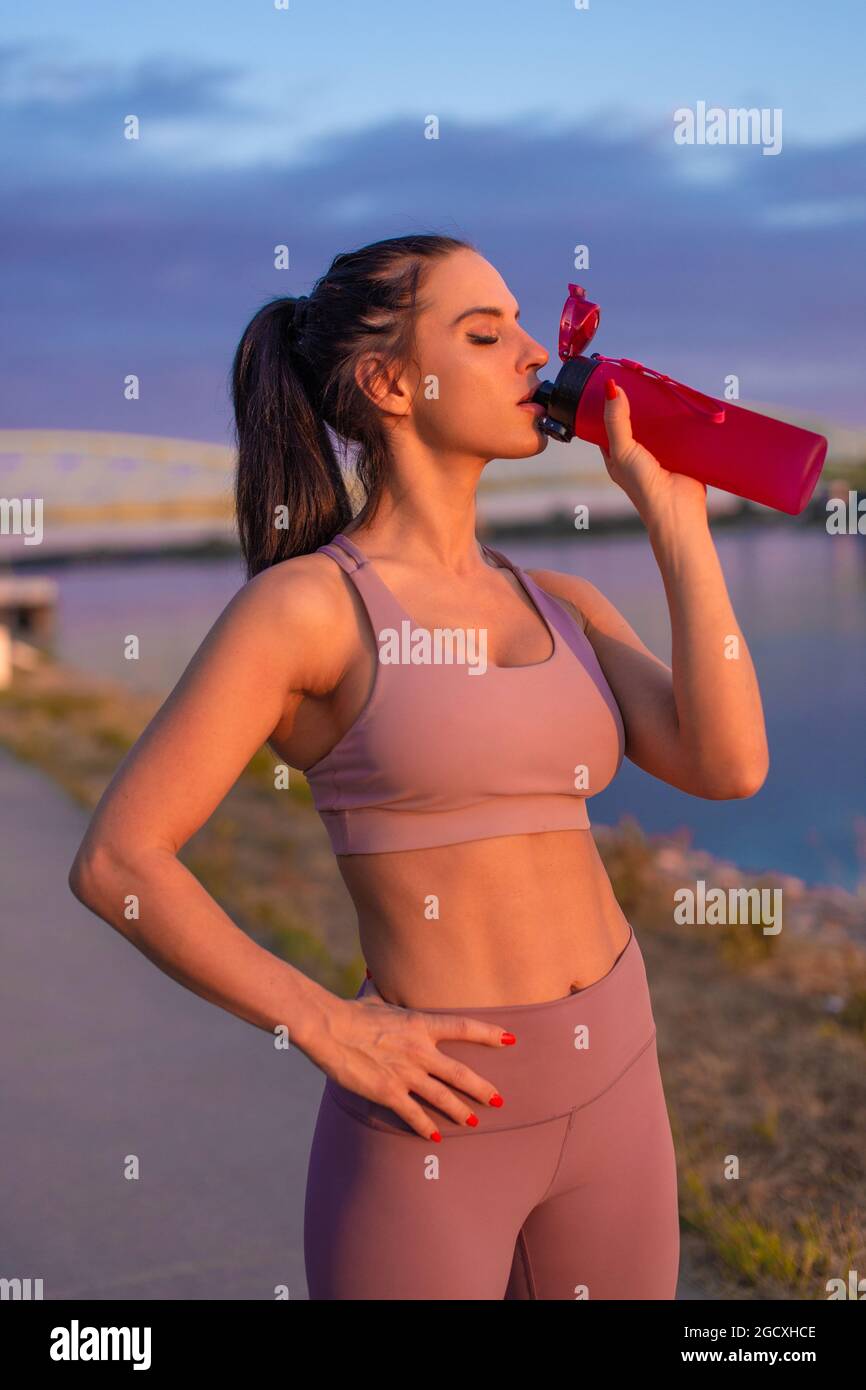 Durstige Frau in Sportkleidung, die am Flussufer Erfrischung aus der Flasche trinkt Stockfoto