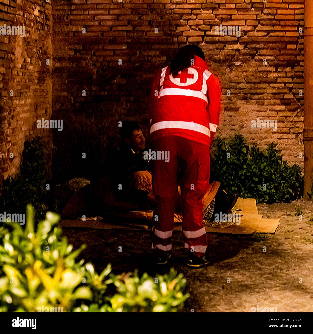 Ein Freiwilliger hilft einem Obdachlosen, der in einer dunklen Ecke der Straße schläft. Eine moderne Gesellschaft sollte den Unglücklichen ein Zuhause bieten. Stockfoto