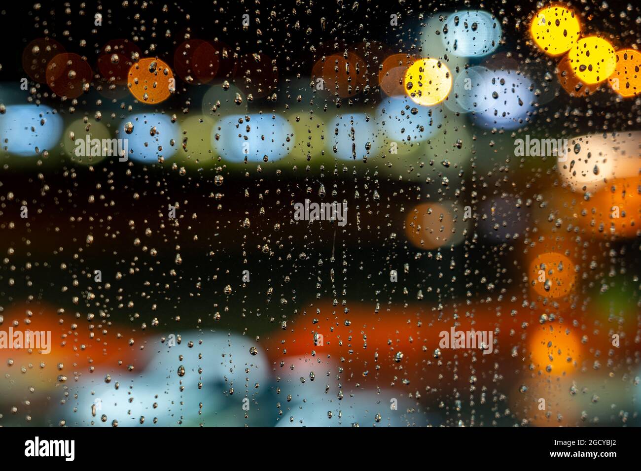 Regentropfen auf einem Fensterglas mit verschwommenen bunten Lichtern im Hintergrund Stockfoto