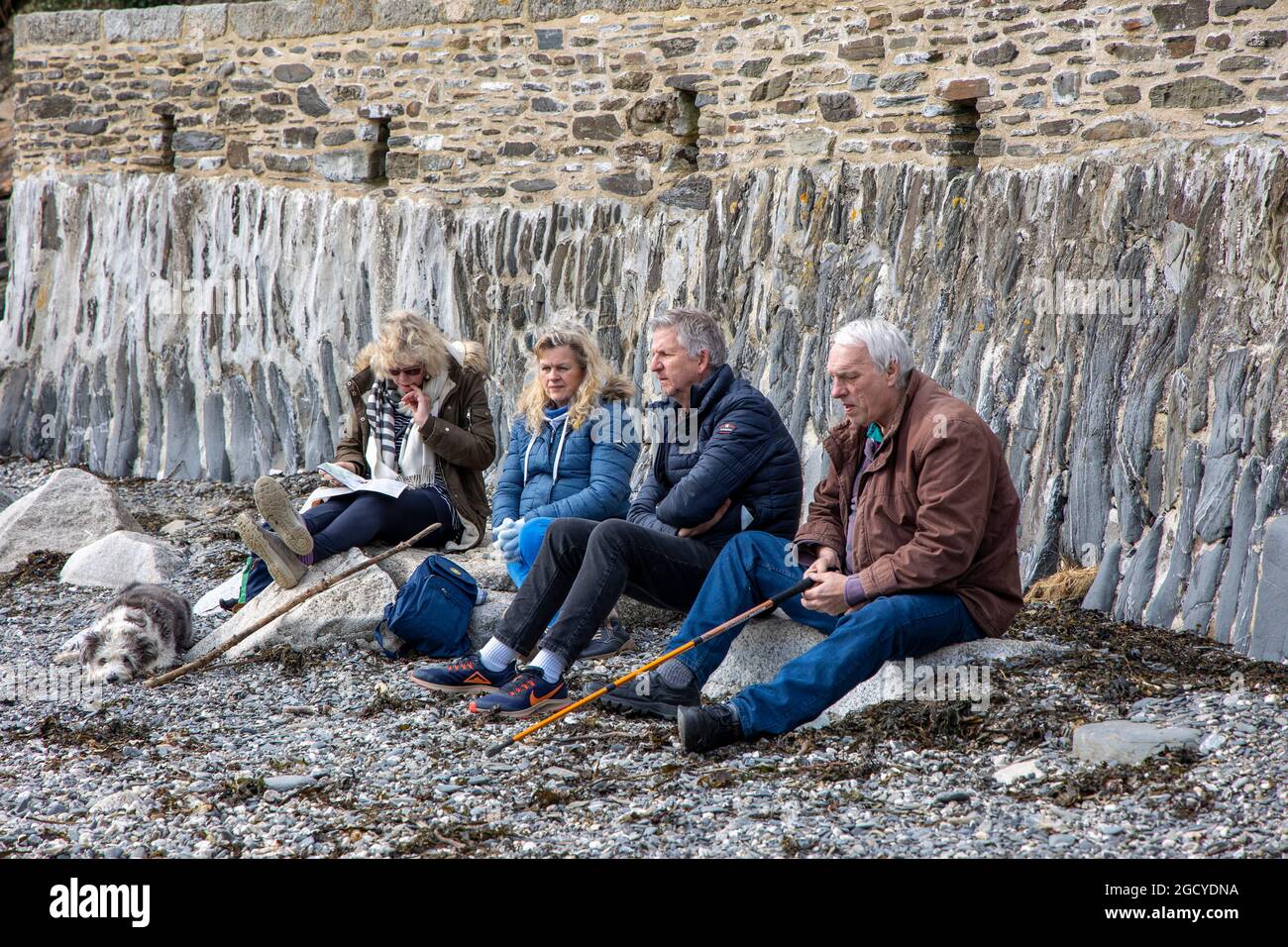 Winter, Durgan Beach, Cornwall. Freunde sitzen in der Kälte am steinigen Strand von Durgan, Helford River, und sehen während der Covid Lockdown gelangweilt aus Stockfoto