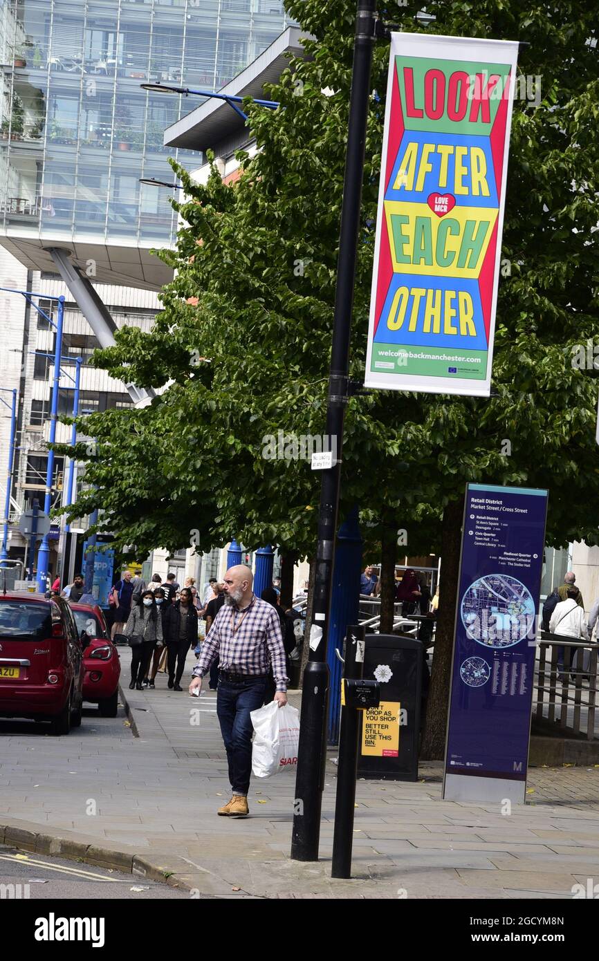 Manchester, Großbritannien, 10. August 2021. Die Menschen gehen an einem lokalen Schild vorbei, auf dem sie aufgefordert werden, sich in Manchester, Großbritannien, gegenseitig zu kümmern. Covid-19- oder Coronavirus-Infektionsraten sinken in Manchester, steigen aber in drei anderen Stadtteilen von Manchester an: Stockport, Bury und Trafford, laut den neuesten Daten von Public Health England. Quelle: Terry Waller/Alamy Live News Stockfoto