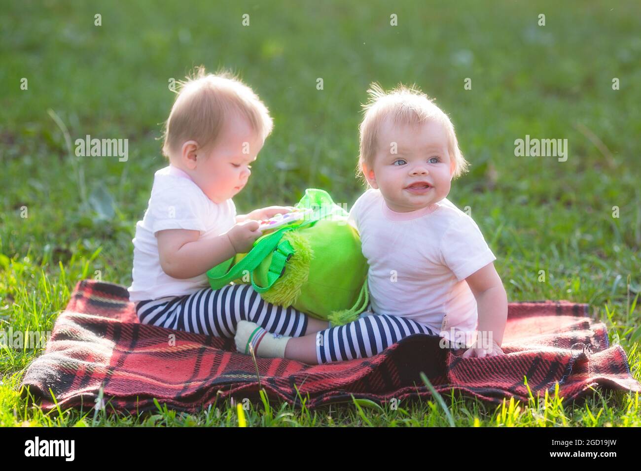 Zwei Kinder an einem sonnigen Sommertag auf dem Rasen mit einem Kinderrucksack. Stockfoto