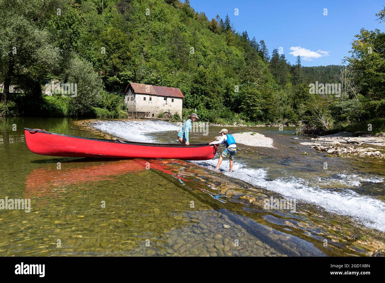 Mutter und Sohn führen ein Kanu an einer alten Mühle entlang eines Wellenbrechers vorbei, der Slowenien und Kroatien über den Fluss Kolpa verbindet Stockfoto
