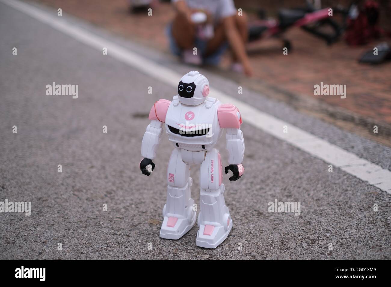 Ein Spielzeugroboter, der von einem Mädchen ferngesteuert wird, bewegt sich über die Straße Stockfoto