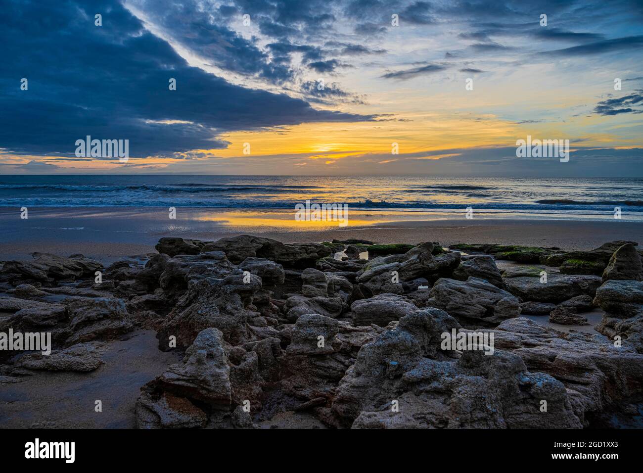 Kontrastierende Meereslandschaft aus dunklen Wolken, hellem Sonnenaufgang, Erde und Himmel und Meer mit Wasser und Felsen. Stockfoto