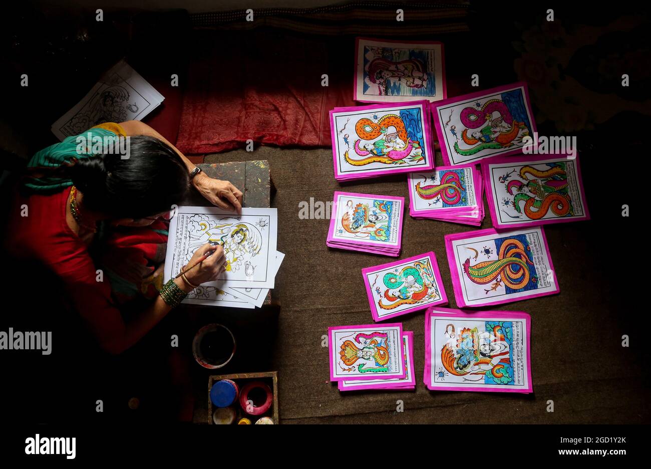 Bhaktapur, Bagmati, Nepal. August 2021. Chet Kumari Chitrakar, 68, populär bekannt als ''Schöpfer der Götter'', bereitet das traditionelle Bild für das bevorstehende Nag Panchami Festival vor, ein hinduistisches Fest für die Anbetung der Schlangengottheit in Bhaktapur, einer Stadt, die auch als ''˜die Stadt der Devotees' in Nepal am 10. August 2021 bekannt ist. Chet Kumari Chitrakar und seine Familie machen weiterhin solche Handdruckbilder für viele Festivals, trotz der geringeren Nachfrage aufgrund des Interesses der Menschen an den modernen Maschinendruckbildern. Chitrakar-Familien sind im Grunde als Maler und Bildhauer in Nepal bekannt, die Götter und Göttinnen darstellten Stockfoto