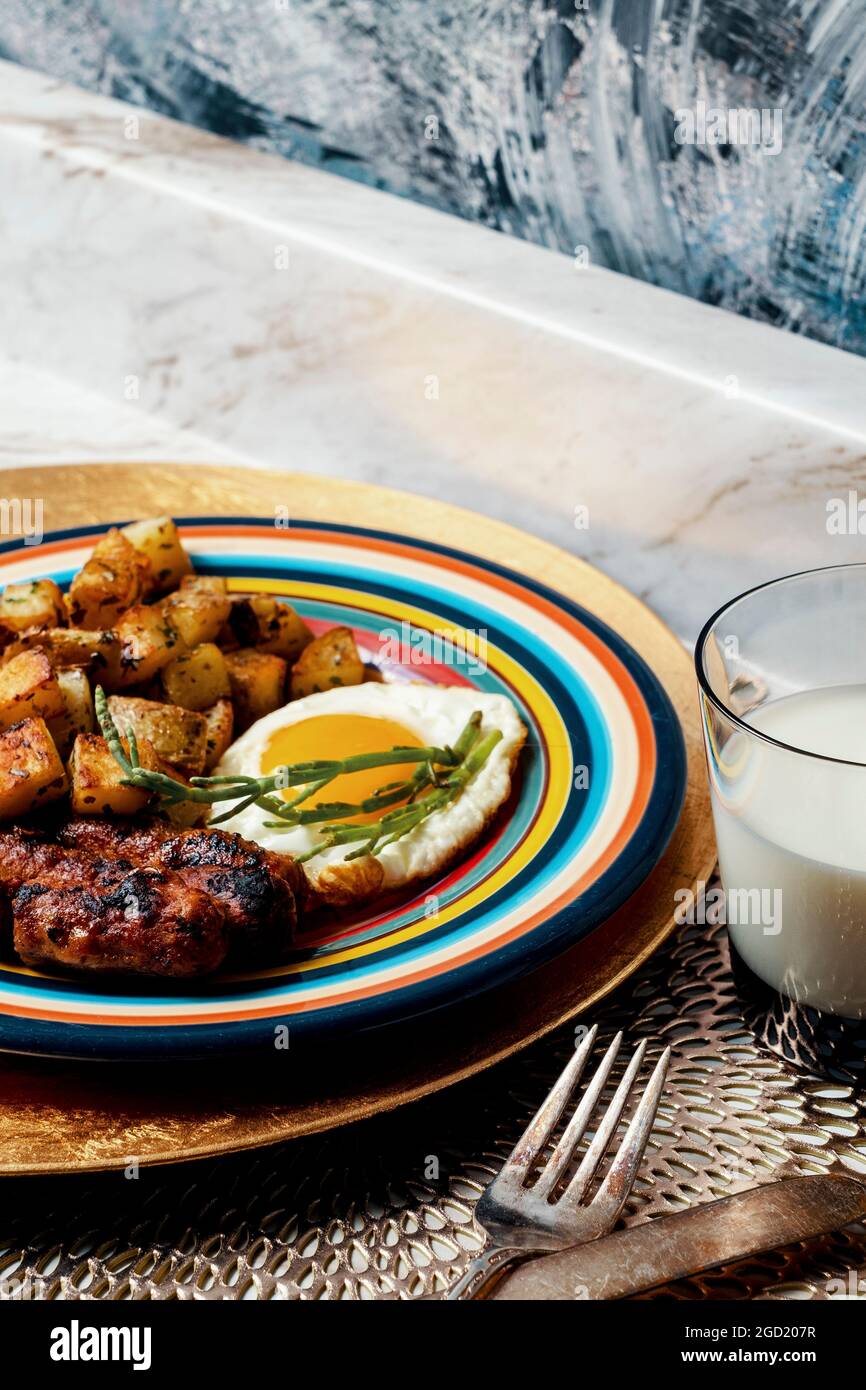 Komplettes amerikanisches Frühstück, gebratene, sonnige Eier, Würstchen, Kartoffeln, O'brien und eine Seebohnengarnitur, serviert mit einem Glas Vollmilch Stockfoto