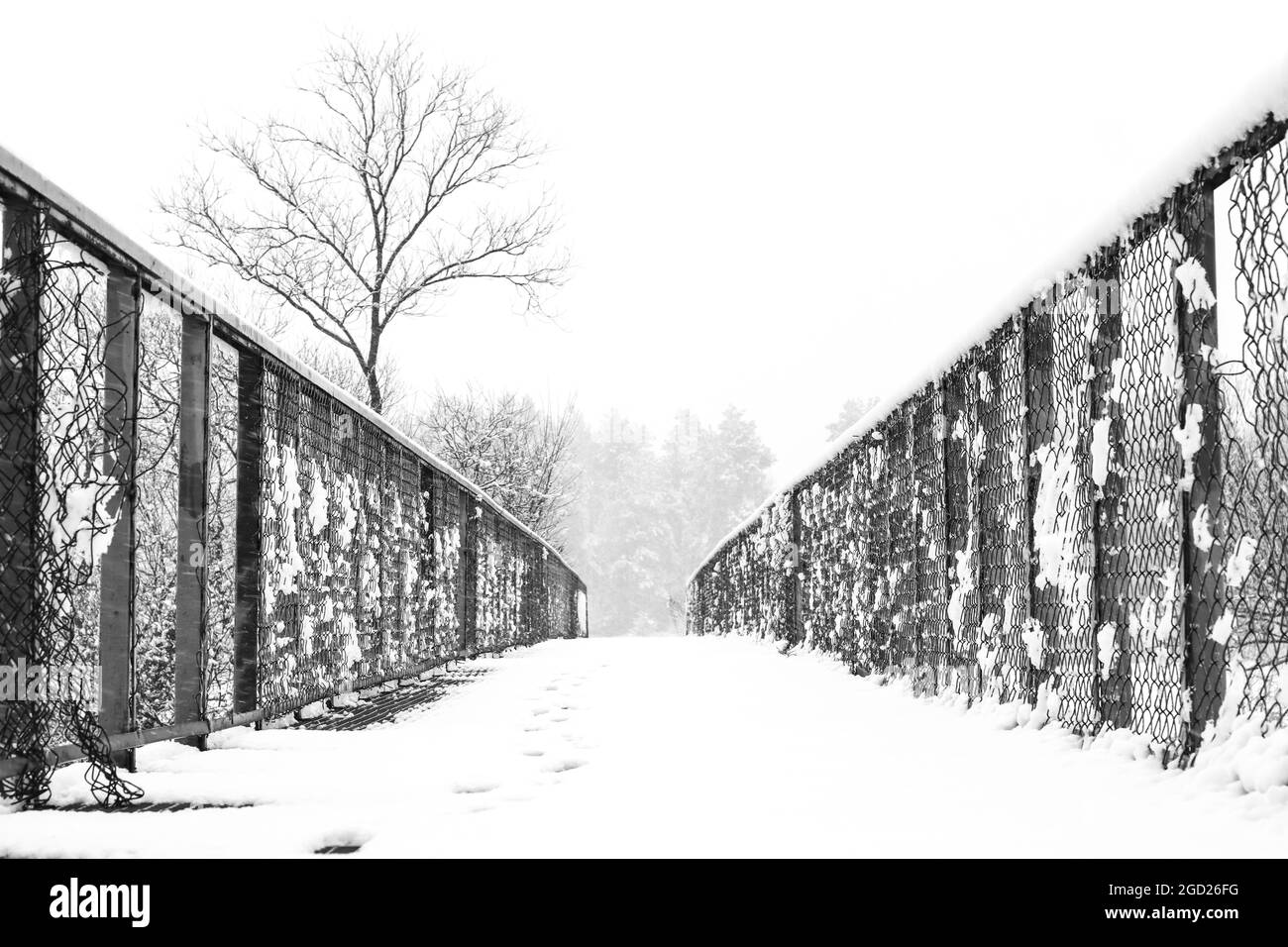 Metallfußbrücke über kleinen Fluss mit Schnee während Schneefall bedeckt führen zu Feld Stockfoto