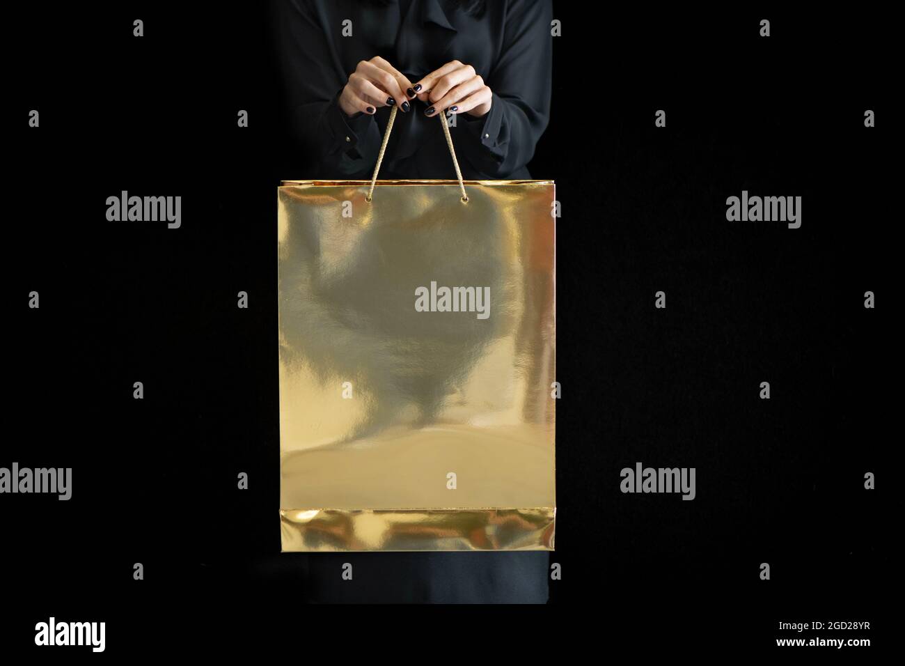 Nicht erkennbare Frau mit goldener Einkaufstasche auf dunklem Hintergrund. Stockfoto
