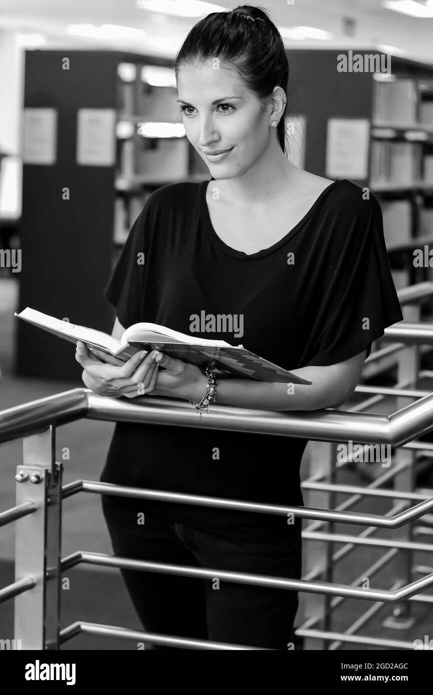 JOHANNESBURG, SÜDAFRIKA - 05. Jan 2021: Eine lächelnde Frau schaut etwas an, während sie ein geöffnetes Buch auf einem Campus hält Stockfoto