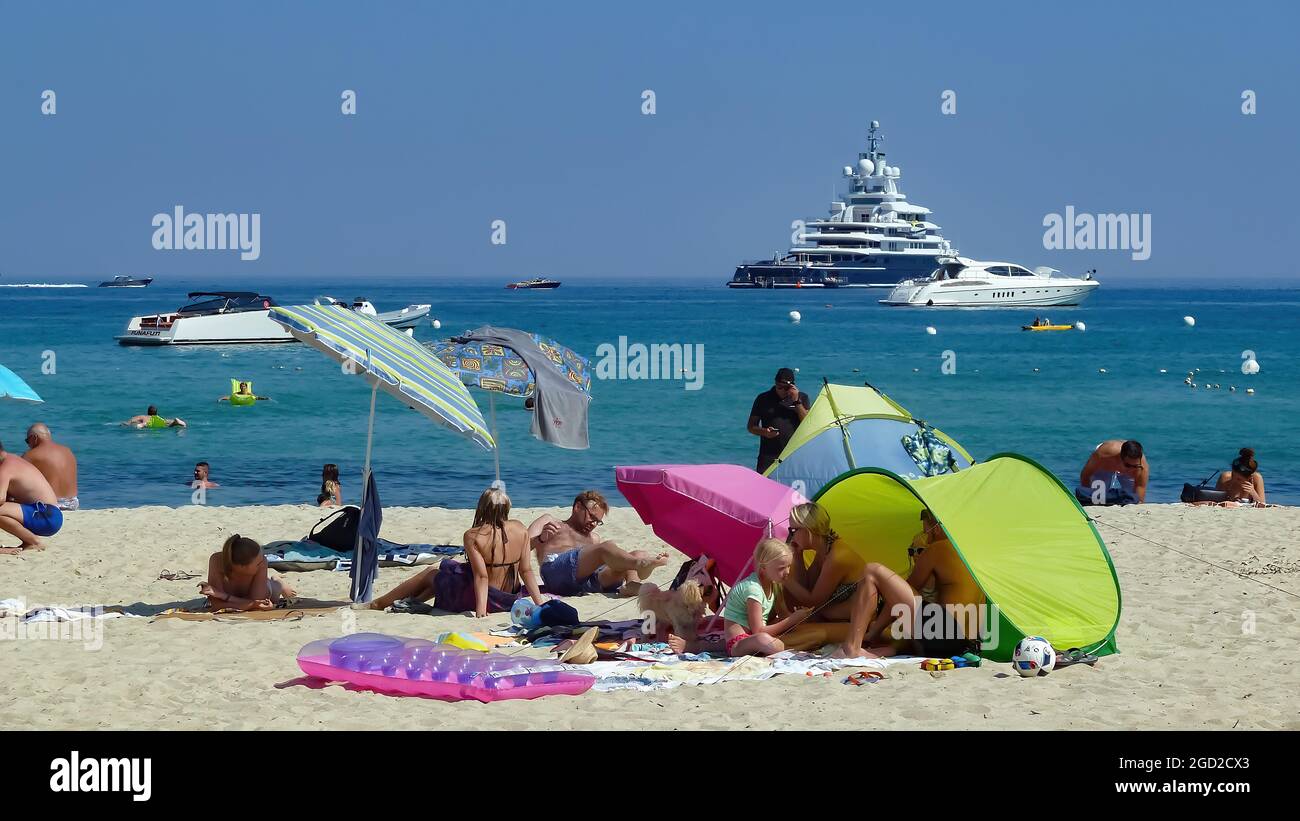 St. Tropez (Plage de pampelonne), Frankreich - Juni 9. 2016: Blick auf Menschen, die sich am Sandstrand entspannen, Mittelmeer mit Yachten Hintergrund (Fokus auf niedrig Stockfoto