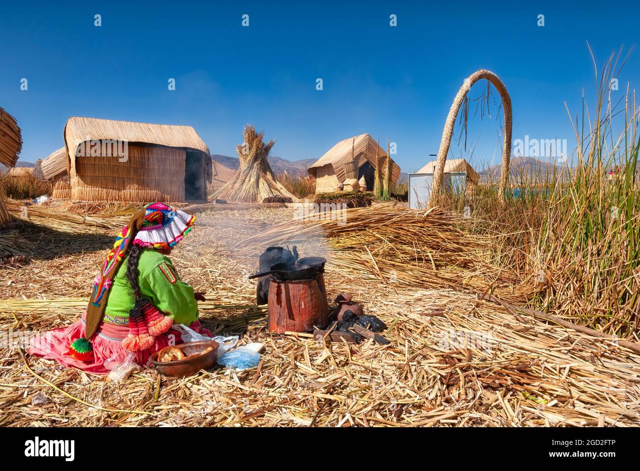 Puno, Peru - 22. August 2010: Eine Uro-Frau in traditioneller Kleidung kocht sitzend. Die Uru sind ein indigenes Volk, das am Titicacasee lebt Stockfoto