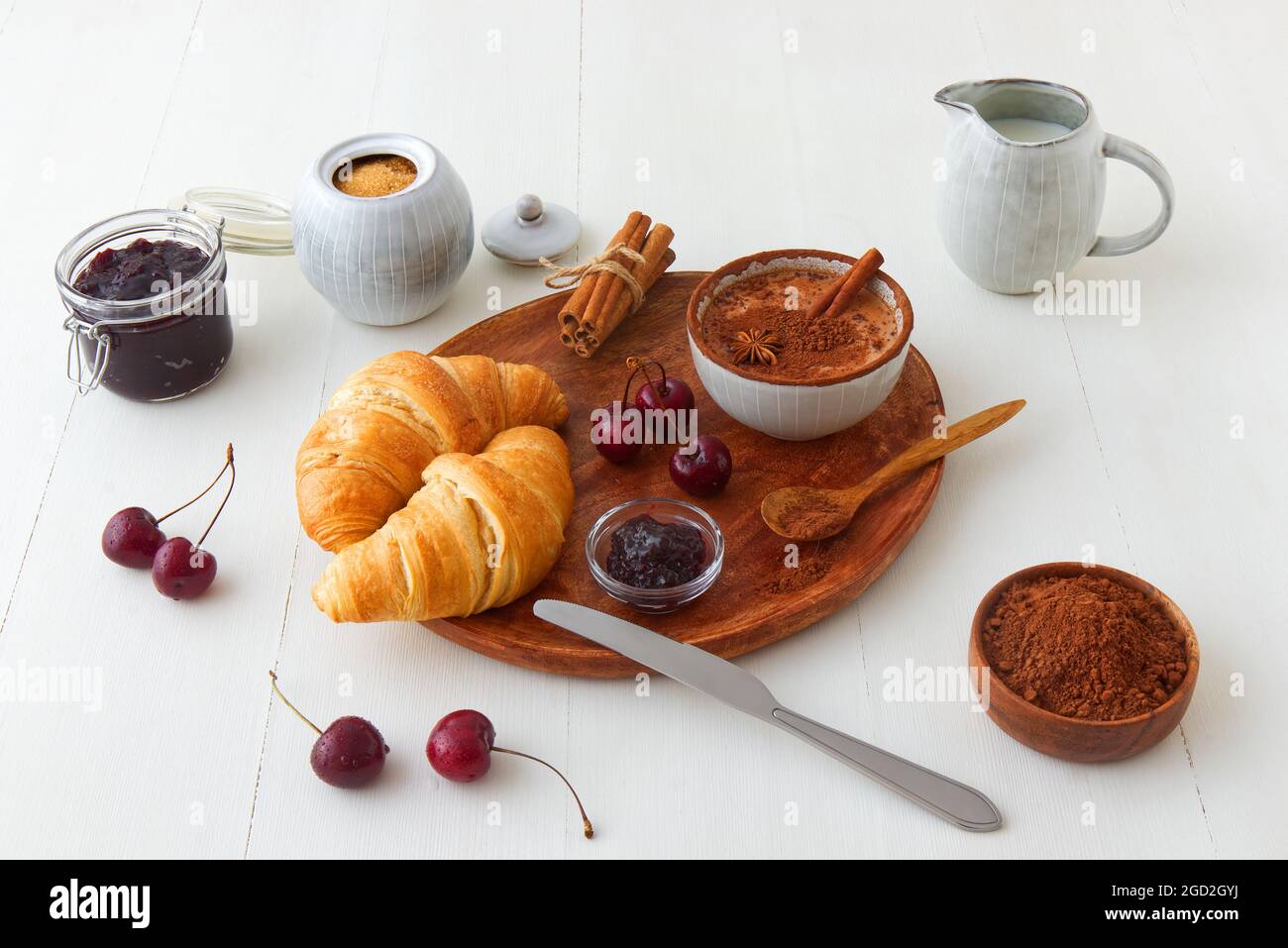 Leckeres gesundes Essen, Frühstück, Brunch oder einfach nur Dessert. Frisch gebackene Croissants mit Marmelade aus der neuesten Kirschernte und heißem Kakao. Weißer Holztisch Stockfoto