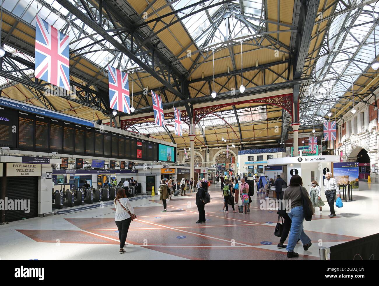 Die Hauptbahnhofstation in Londons Victoria Station. Zeigt die Abflugtafel, die Ticketbarrieren und das viktorianische Gewölbedach. Stockfoto