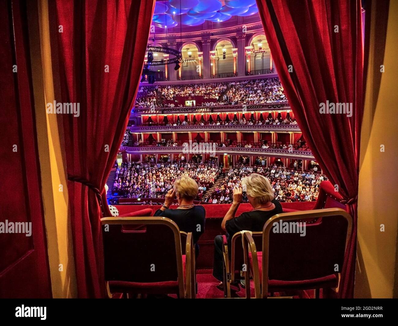 ALBERT HALL BOX PERFORMANCE INTERIOR zwei Damen beobachten eine Aufführung durch eine Opernbrille in einer privaten Box mit rotem Samt und Plüschvorhängen in der Royal Albert Hall Kensington London Stockfoto