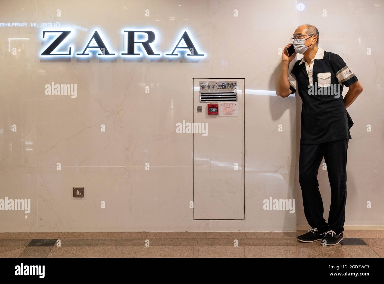 Hongkong, China. August 2021. Ein Mann benutzt ein Smartphone neben dem spanischen multinationalen Bekleidungsdesign-Einzelhandelsunternehmen von Inditex, dem Zara-Logo in Hongkong. Kredit: SOPA Images Limited/Alamy Live Nachrichten Stockfoto