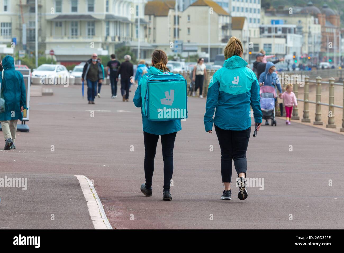 Weibliche mitarbeiter von deliveroo, die entlang der Strandpromenade, hastings, East sussex, großbritannien, spazieren Stockfoto