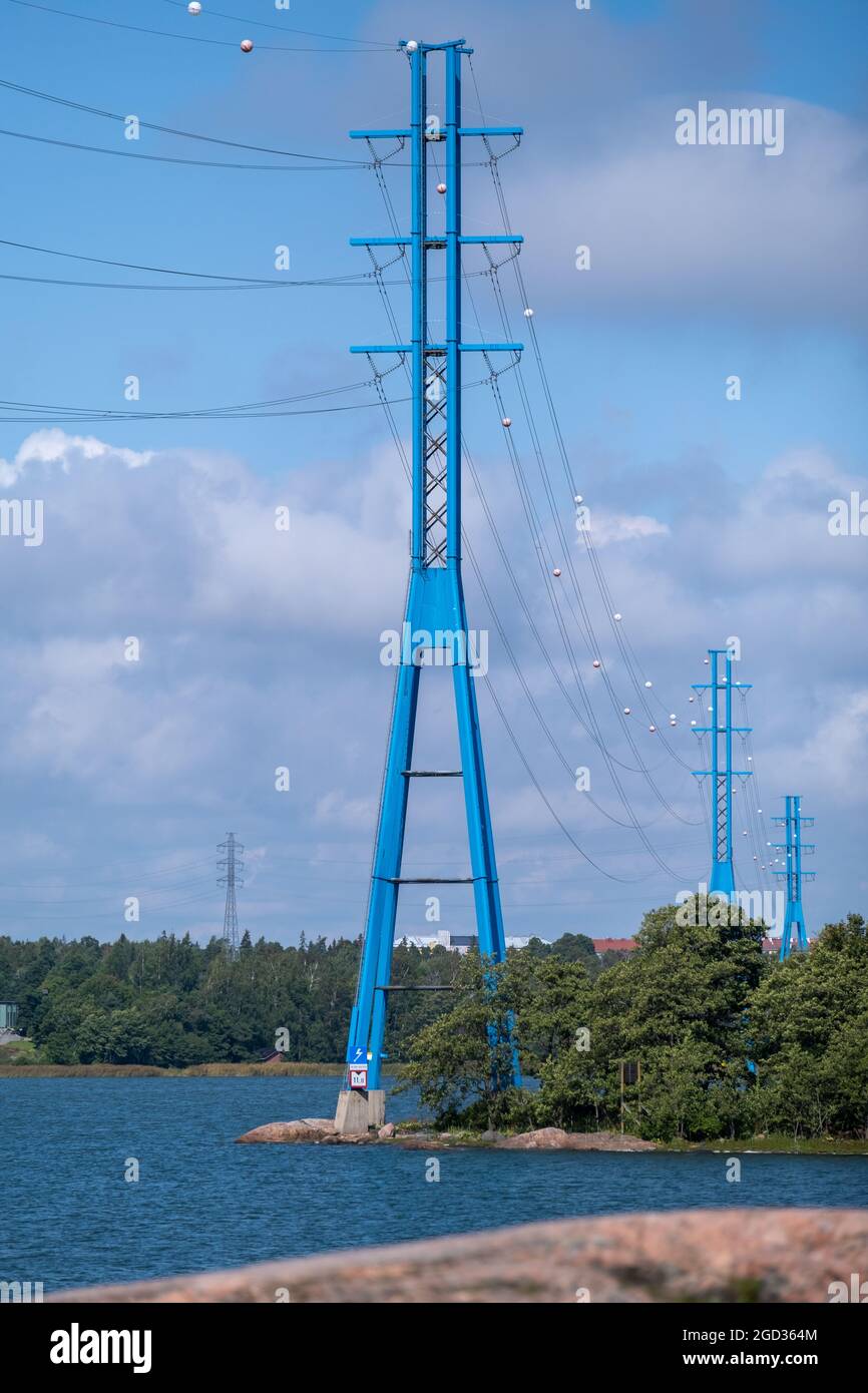 Helsinki / Finnland - 10. AUGUST 2021: Eine Reihe moderner Hochspannungsmasten am Ufer gegen den bewölkten Himmel. Stockfoto