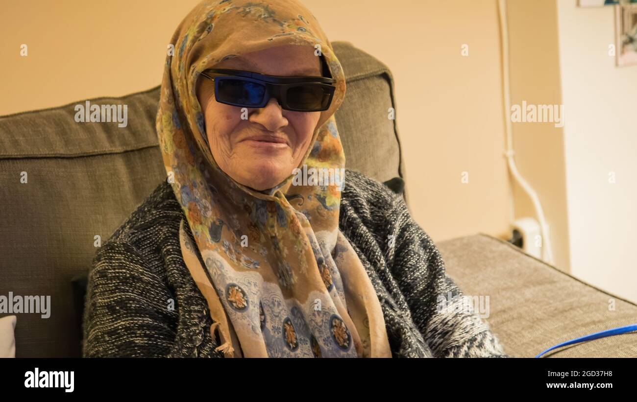 Ältere muslimische Frau mit 3D-Brille beim Fernsehen. Sie ist glücklich und genießt die Show. Konzept der älteren Frau, die Technologie nutzt Stockfoto