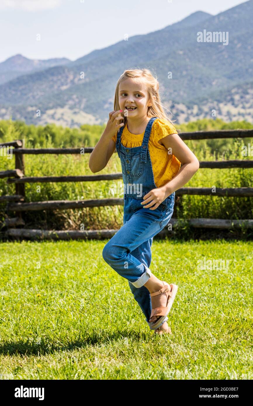 Junges Mädchen spielt und läuft im grasbewachsenen Hof Stockfoto