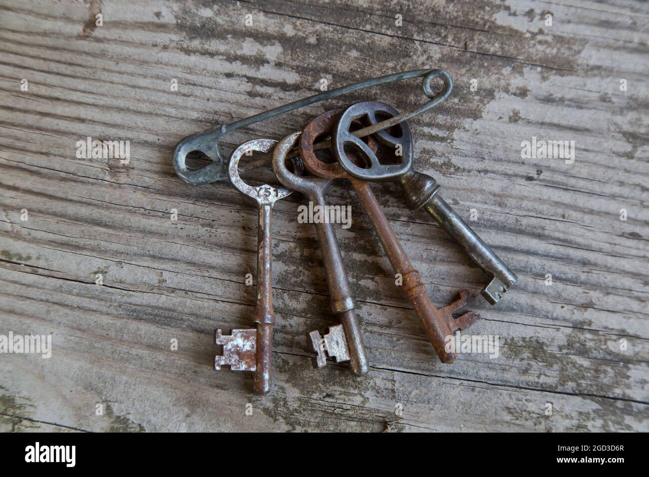 Klassische Metallschlüssel, die mit einer Sicherheitsnadel an einer Holzwand befestigt sind. Stockfoto